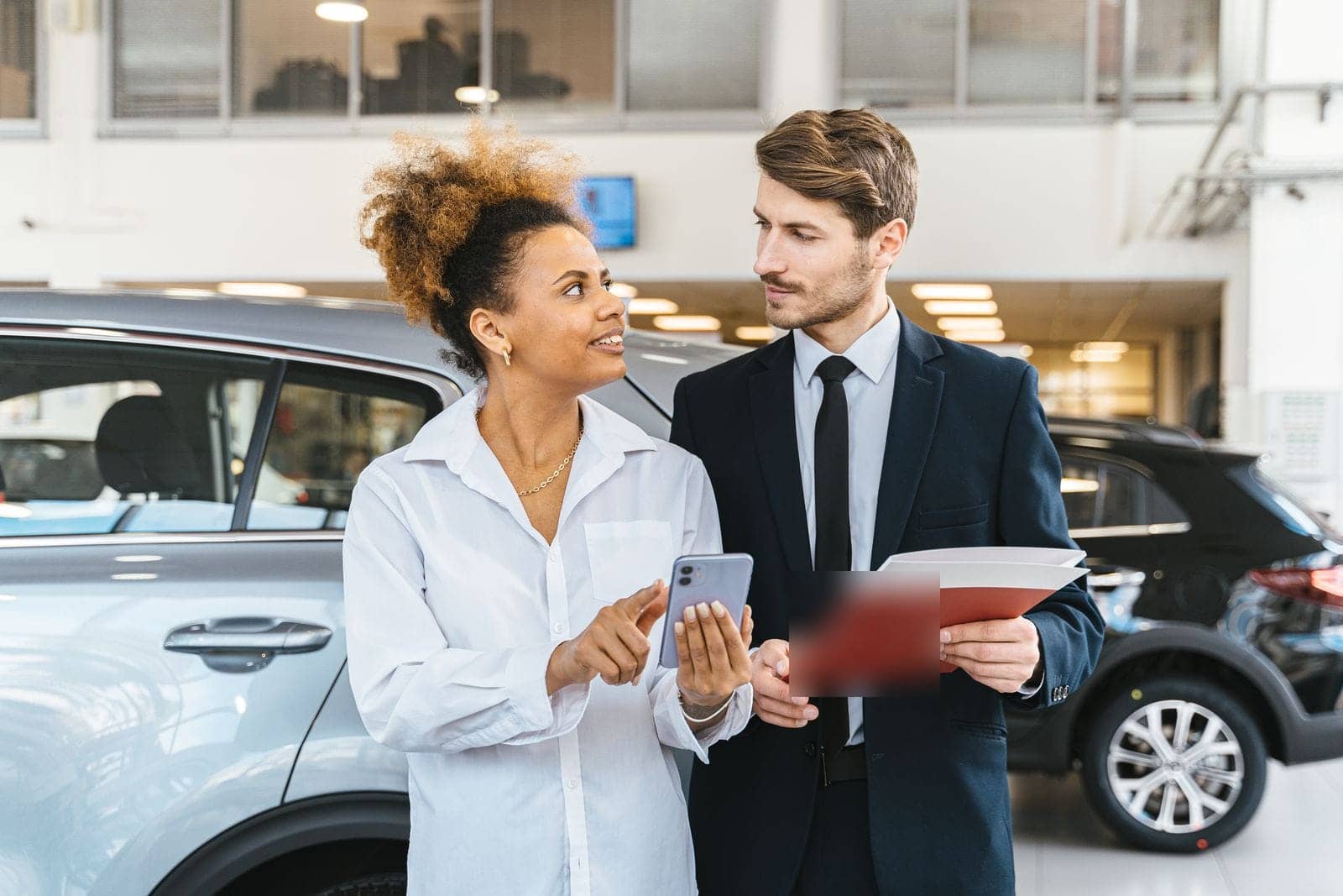 Vendedor mostrando informações no celular a uma cliente ao lado de um SUV prata